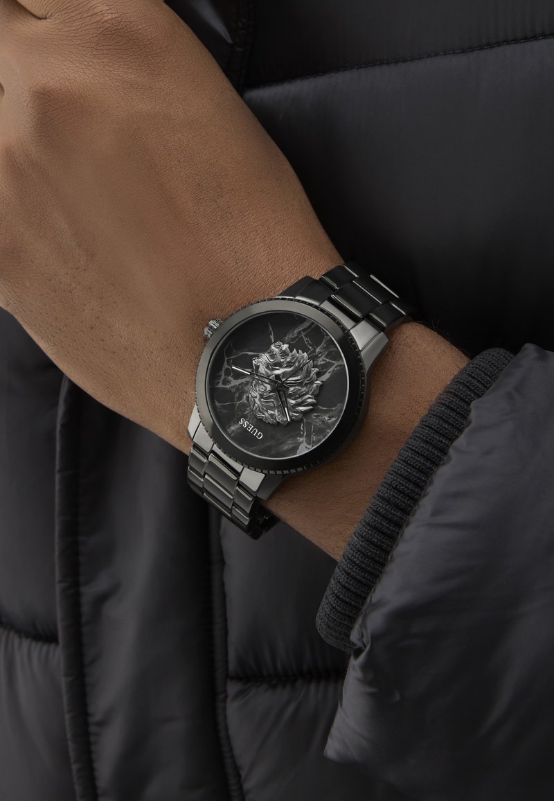 Zwart metalen horloge met een gestructureerde zwarte marmeren wijzerplaat met een reliëfontwerp. Zilveren wijzers en een schakelband maken de uitstraling compleet.