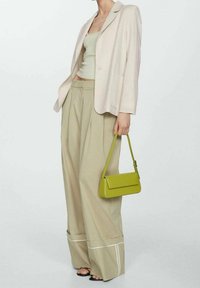 Béžové sako přes zelený žebrovaný top, doplněné béžovými širokými kalhotami s bílým lemem a malou limetkově zelenou kabelkou.