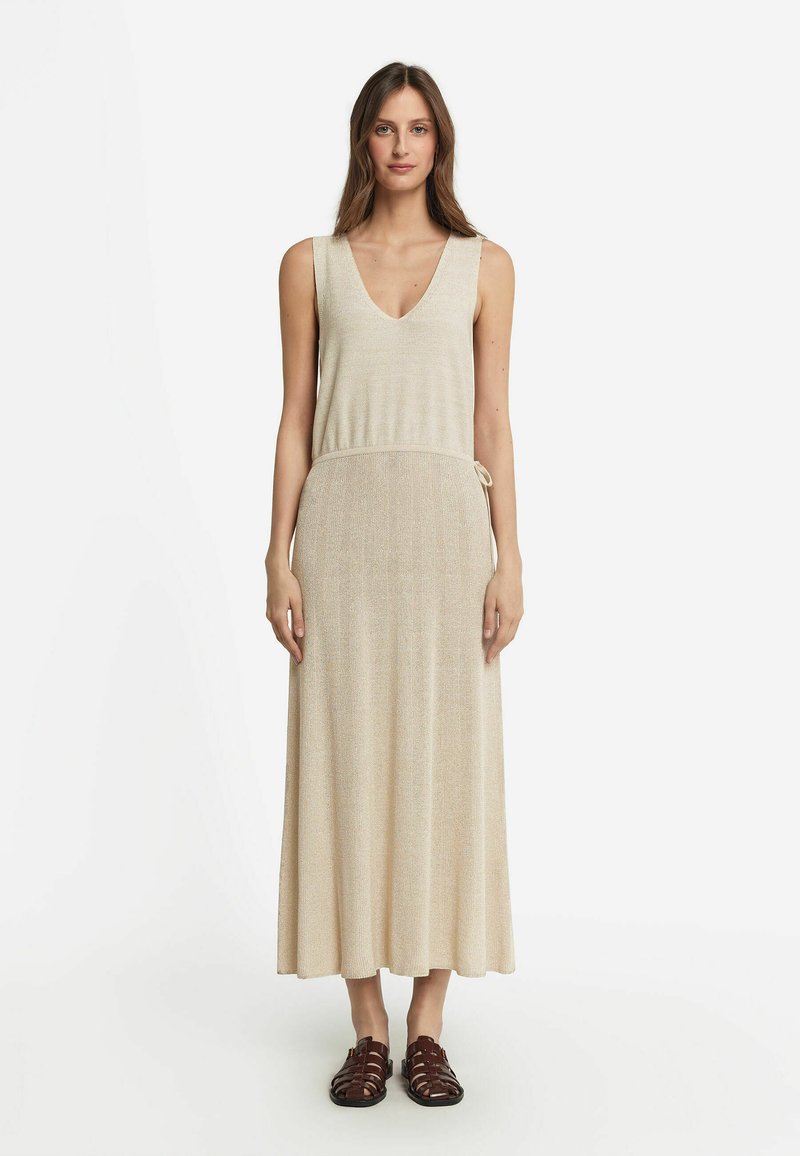 Beige maxiklänning med V-ringning, ärmlös design, texturerat tyg och knytning i midjan. Bärs med bruna sandaletter med remmar.