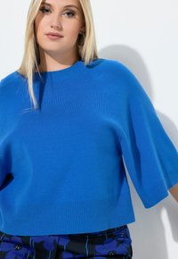 Blauer Strickpullover mit geripptem Ausschnitt und Saum, kurzen Ärmeln und lockerem Schnitt. Glatte Textur und lebendige Farbe.