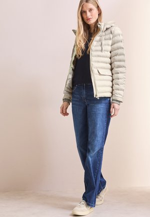 Doudoune beige clair avec capuche et design matelassé horizontal, associée à un jean large bleu et des baskets crème.