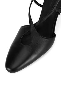 Melna ādas kurpe ar norādītu pirkstu un izgriezumu dizainu. Aprīkota ar šaurām pārklājošām siksnām un gludu tekstūru augšējā daļā.