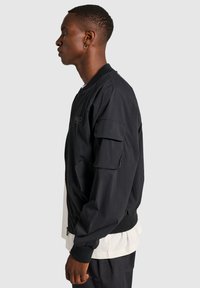 Czarna kurtka bombowca z zapięciem na suwak, ściągaczami na mankietach i kieszeniami na ramionach. Wykonana z lekkiego materiału, z delikatnym logo marki.