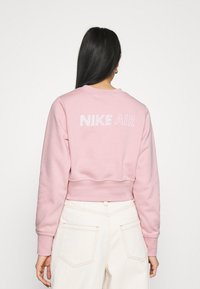 Felpa cropped rosa con scollatura rotonda, polsini a coste e retro caratterizzato da un testo in rilievo "NIKE AIR". Tessuto morbido.
