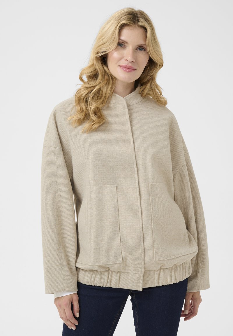 Sweat-shirt beige en tissu texturé, avec un col montant, deux poches avant et un ourlet resserré. Coupe décontractée avec des épaules tombantes.
