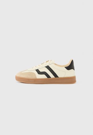 Lace-up sneakers featuring a cream upper with black stripes and a suede toe cap, complemented by a brown rubber sole.