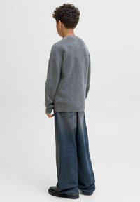 Pelēks adīts džemperis ar apaļu dekoltē, apvienots ar brīvi piemērotiem tumšas krāsas džinsiem un melniem potīšu zābakiem. Vienkārša, brīva piegriezuma dizains.