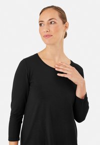 Czarna bluzka z długim rękawem i okrągłym dekoltem, wykonana z gładkiego materiału. Posiada dyskretne szwy i luźny krój, noszona przez modelkę.