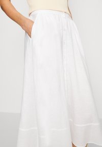Falda de lino blanca con diseño acampanado, con botones delanteros y bolsillos laterales. Textura suave con un detalle en el dobladillo.