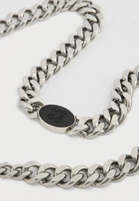 Collana a catena d'argento con maglie spesse, finitura lucida e una targhetta ovale nera con "HUGO" inciso al centro.