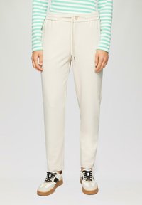 Beige joggerbroek met elastische tailleband en trekkoord. Glad textuur, taps toelopende fit, zijzakken, gecombineerd met zwart-witte sneakers.