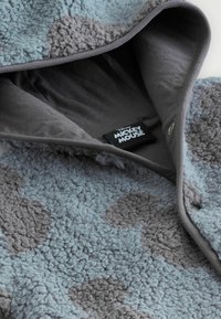 Sudadera de felpa en azul claro y gris, con una superficie suave y texturizada que presenta un patrón de manchas gris oscuro. Incluye un forro gris y una etiqueta.