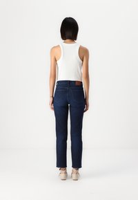 Jeans de ganga azul escuro com pernas retas e dois bolsos traseiros, combinados com uma camisola branca de alças com relevo e sapatos de salto bejes.