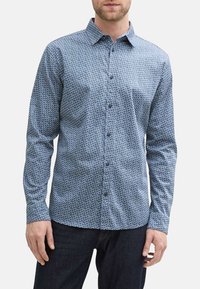 Blauw met patroon knoopshirt met lange mouwen, gemaakt van een gestructureerde stof. Heeft een kraag en donkere knopen, gedragen met donkere jeans.