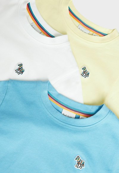 Tre t-shirt a maniche corte in cotone blu, bianche e gialle; ognuna presenta un piccolo logo di zebra ricamato e un collo a righe colorate.