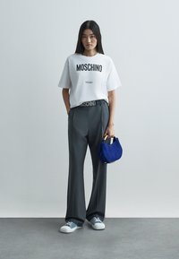 Valge T-särk musta "Moschino Milano" kirjaga, hallid laiad püksid, sinine seemisnahast käekott ning sinised ja valged tossud.