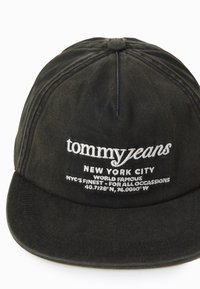 Căciulă de baseball neagră din material textil, cu bor curbat. Se remarcă printr-un text alb brodat care include "tommy jeans" și coordonate, având șase panouri cusute.