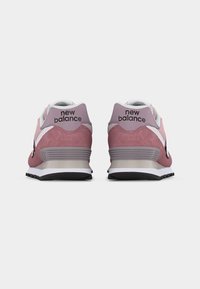Paire de baskets New Balance roses et blanches vues de dos sur un fond gris clair uni.