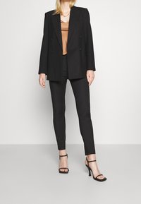 Svart dubbelknäppt blazer med vadderade axlar, kombinerad med åtsittande svarta byxor och svarta sandaletter med remmar. Satsing på en brunt satin topp under.