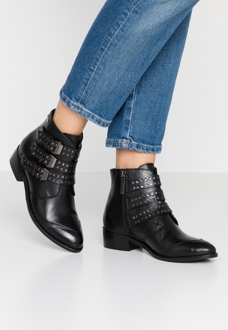 Černé kožené kotníkové boty se třemi nastavitelnými přezkami a kovovými hroty, s nízkým podpatkem a špičatou špičkou.