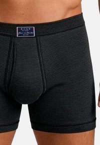 Mustat raidalliset bokserit joustavasta kankaasta. Niissä on tiukka vyötärönauha, jossa on merkki, kapeat lahkeet ja tukevasti muotoiltu etutasku.