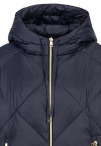 Navy gewatteerde pufferjas met hoge kraag, voorzien van een gouden ritssluiting en elastische trekkoord. Zachte, gladde stof met een gestructureerd patroon.