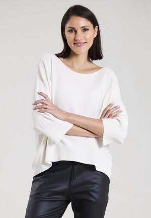Weißer, gerippter Strickpullover mit weitem Ausschnitt und 3/4-Ärmeln, kombiniert mit schwarzer, enganliegender Hose. Weiche Textur, lässiges Design.