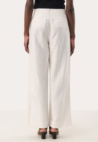 Pantalon blanc à jambes larges avec des fines rayures verticales, doté d'une taille mi-haute, d'une texture lisse et de poches arrière discrètes. Sandales à talons portées.