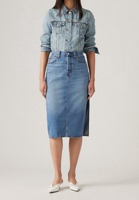 Ljusblå denimjacka med bröstfickor och knäppning, i kombination med en matchande denim-midirubrik med sidoklyvning och bältesöglor.