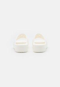 Croc blancs avec sangle arrière, fabriqués en matériau léger. Dotés de trous de ventilation circulaires et d'un semelle texturée pour le confort.