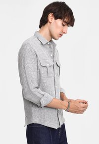 Camicia a bottoni grigia con motivo, due tasche sul petto, maniche lunghe arrotolate, realizzata in un tessuto texturizzato, dotata di colletto standard.