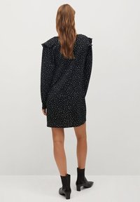 Robe noire à pois blancs, avec des détails froncés aux épaules et des manches longues, associée à des bottines noires.