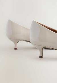 Béžové lakované lodičky s elegantním designem, špičatou špičkou a nízkým, taperovaným podpatkem. Hladký povrch s lesklým finišem.