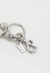 Silver keychain with a rounded clip, link chain, and a rectangular tag engraved with "COACH." Smooth metallic finish, compact design.