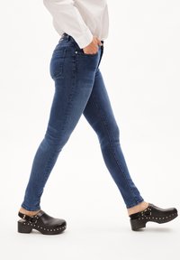Modré džíny skinny s běžným praním, obsahující přední kapsy a vyšívané detaily, v kombinaci s černými dřeváky se stříbrnými cvoky.