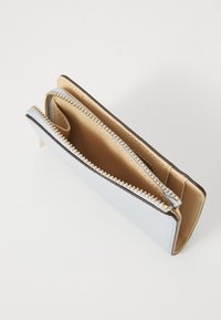 Porte-monnaie zippé bleu clair avec un extérieur texturé et une fermeture éclair dorée. L'intérieur dispose d'un revêtement en tissu beige et de fentes pour cartes.