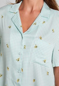 Lichtblauw geruit overhemd met een notch kraag, korte mouwen en gele bloemenborduursels. Bevat een borstzakje en een knoopsluiting.