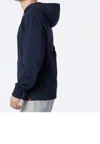 Felpa con cappuccio blu navy realizzata in morbido tessuto, con tasca a canguro, polsini a costine e un piccolo etichetta rossa sul fondo.