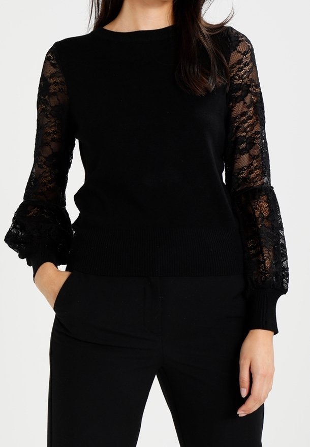 Pull noir avec des manches longues en dentelle, des poignets et un ourlet côtelés. Le corps est en tricot noir uni. Design facile à porter ; minimalisme dans les détails.