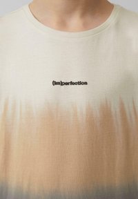 Kurzärmeliges Baumwoll-T-Shirt mit cremefarbenem Grundton und einem Farbverlauf im Batik-Stil in Beige. Text "(im)perfection" in Schwarz aufgestickt.