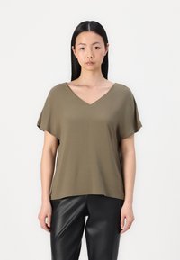 T-shirt vert olive à col en V et à manches courtes, fabriqué en matériau doux. Associé à un pantalon en simili cuir noir, créant une silhouette décontractée.