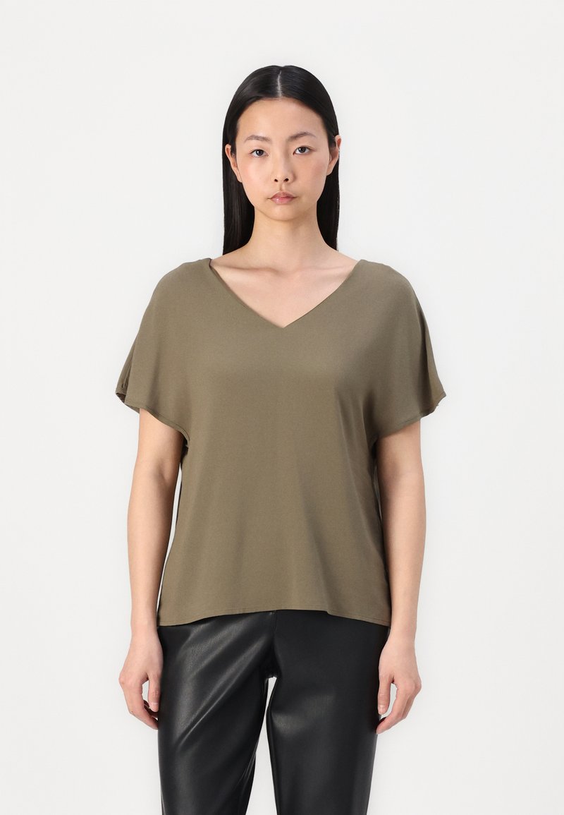 T-shirt vert olive à col en V et à manches courtes, fabriqué en matériau doux. Associé à un pantalon en simili cuir noir, créant une silhouette décontractée.