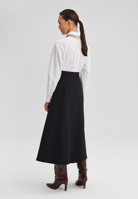 White long-sleeve blouse with a collar, paired with a high-waisted black skirt. Brown knee-high heeled boots complete the outfit.