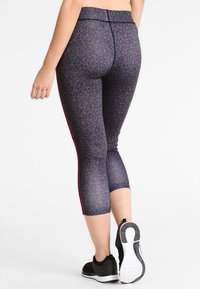 Svarta och grå leggings med geometriskt mönster, en kort design och röda sidodetaljer, tillsammans med svarta träningsskor.