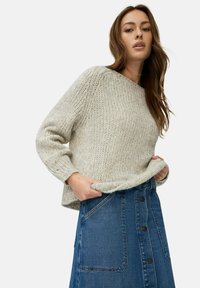 Pull en maille gris clair avec une surface texturée, associé à une jupe en denim dotée de boutons sur le devant et de poches latérales.