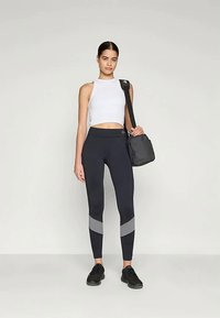 Feszes fehér crop top, fekete leggings szürke részletekkel és fekete sneakers. Egy kis fekete válltáska egészíti ki az atletikus megjelenést.