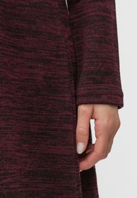 Abito in maglia di un profondo bordeaux con motivo testurizzato. Maniche lunghe aderenti. Dettagli a mano sulla cucitura laterale, che evidenziano la vestibilità comoda e la libertà di movimento.