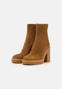Brown suede ankle boots with high block heels, rounded toes, and ankle height. Zipper closure on the side, textured sole detail.