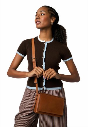 Hnědý žebrovaný svetr s krátkými rukávy a světle modrými volánky, zapínání na knoflíky, doplněný pruhovanými kalhotami a hnědou koženou kabelkou přes rameno.