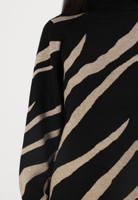 Schwarzer Rollkragenpullover mit einem strukturierten, beige-gestreiften Zebramuster. Hat lange Ärmel und einen taillierten Kragen, hergestellt aus weichem Stoff.